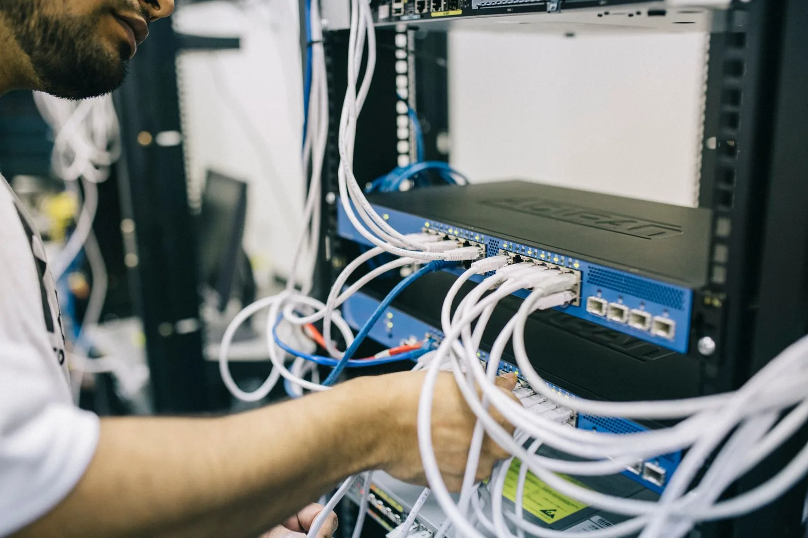 Technician's hands connecting ethernet cables to a network switch in a rack